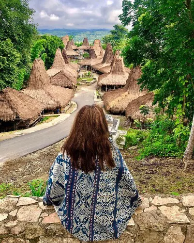 A woman in an ikat wrap looking out over a traditional Sumbanese village